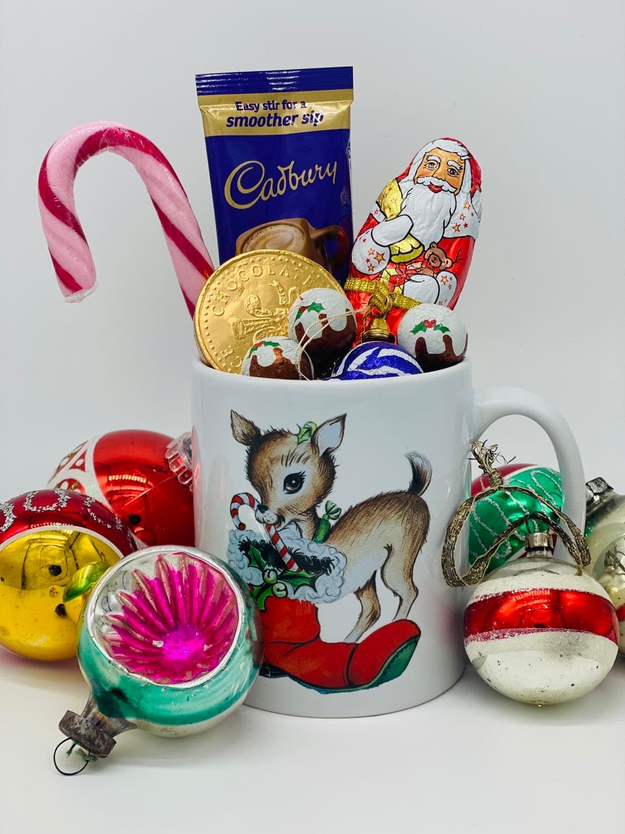 Christmas mug gift filled with chocolates and a candy cane with vintage baubles surrounding the mug.