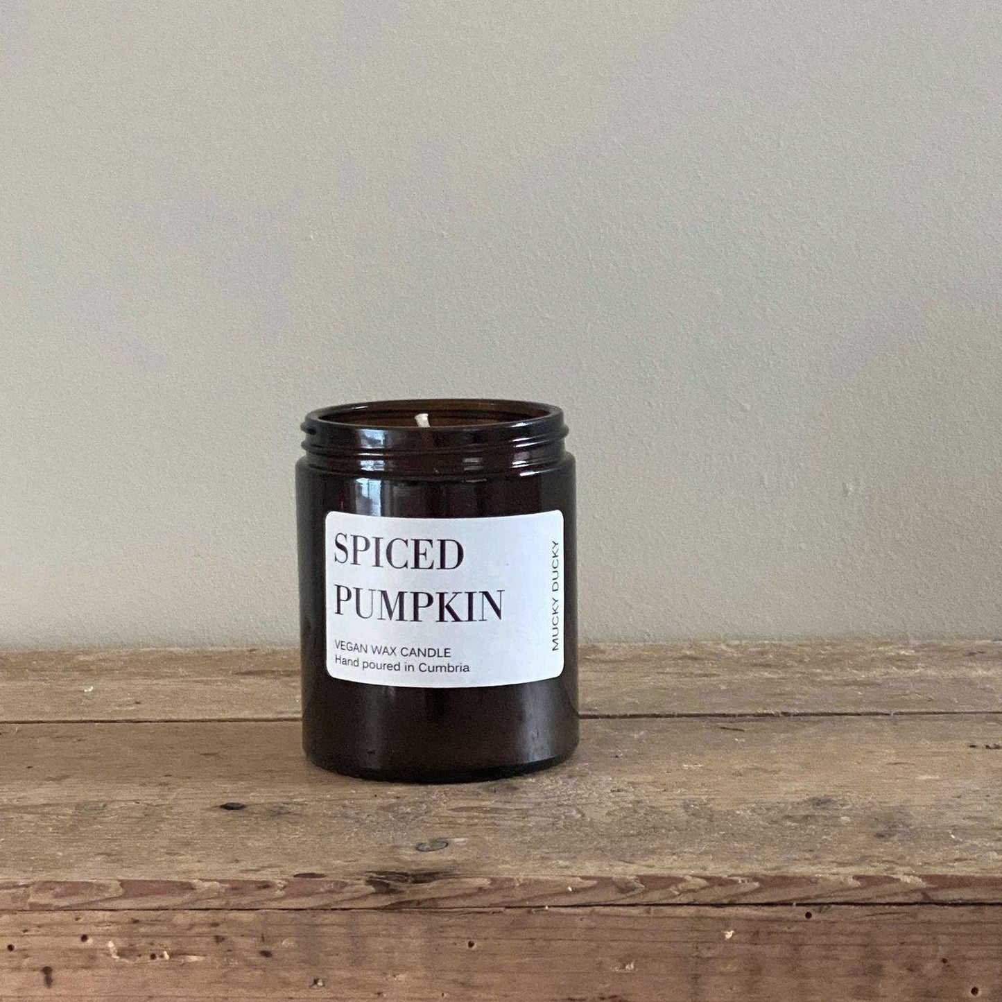 Spiced pumpkin container candle in an amber glass jar. Label says Spiced Pumpkin vegan wax candle, hand poured in Cumbria